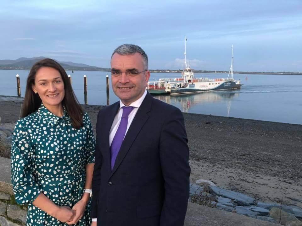 Picture of Senator Erin McGreehan in a green and white patterned dress standing beside Minister Dara - Minister of State in the Department of Enterprise, Trade and Employment, who is wearing a black suit, white shirt and purple tie standing with Carlingford Lough, Co. Louth in the background.