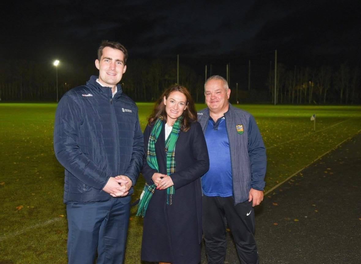 Minister Jack Chambers standing beside Senator Erin McGreehan and Chairman of St Marys GFC, Ardee Mickey Rooney outside St. MAry's GFC Gaelic Grounds