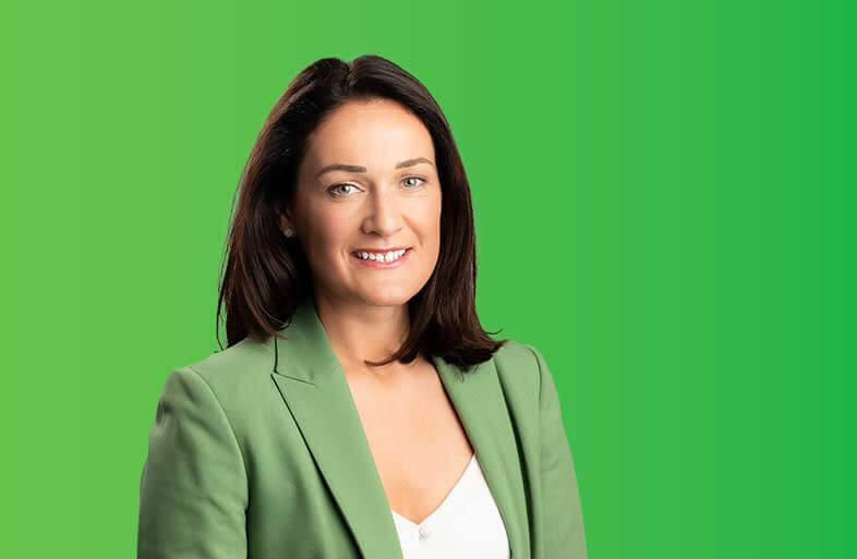 Picture of Erin McGreehan T.D. with a green background. She is wearing a green blazer and white top.