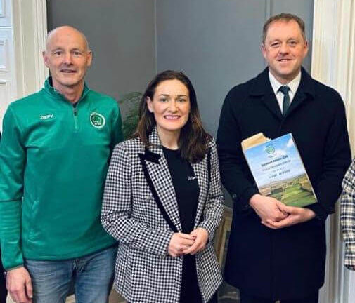 Photo of former Glenmore A.C. Chairman Kenneth McBride wearing a Glenmore A.C. half zip in dark green, standing beside Senator Erin McGreehan who is wearing a black and white blazer. Minister Thomas Byrne is standing to the right of Erin, wearin a black coat, white shirt and a green tie.